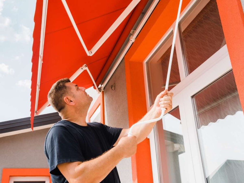Someone carefully inspects the fabric and structure of a red awning,